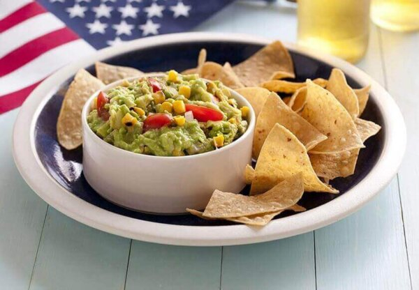 Guacamole com chips de tortilla em um prato com bandeira americana ao fundo