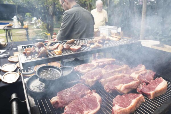 Churrasco Tradicional Paulista - Carnes sendo grelhadas em uma churrasqueira com pessoas ao fundo