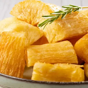 Prato com mandioca frita dourada e crocante, decorada com ramo de alecrim fresco sobre fundo claro