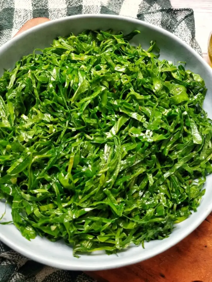 Tigela branca com couve fatiada em tiras finas e temperada, servida em mesa com toalha xadrez verde e branca