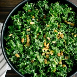 Salada de couve kale verde em tigela preta com pinhões tostados e queijo ralado