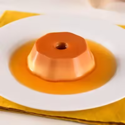 Pudim de caramelo em formato de flan servido em prato branco com calda ao redor