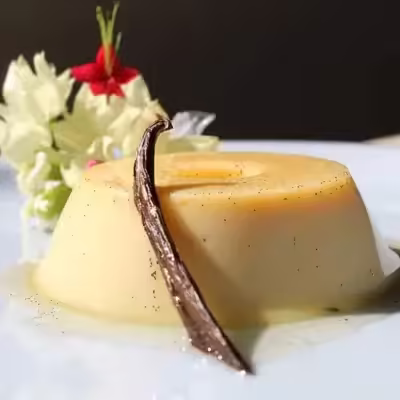Pudim de baunilha com fava de baunilha sobre prato branco com flores ao fundo