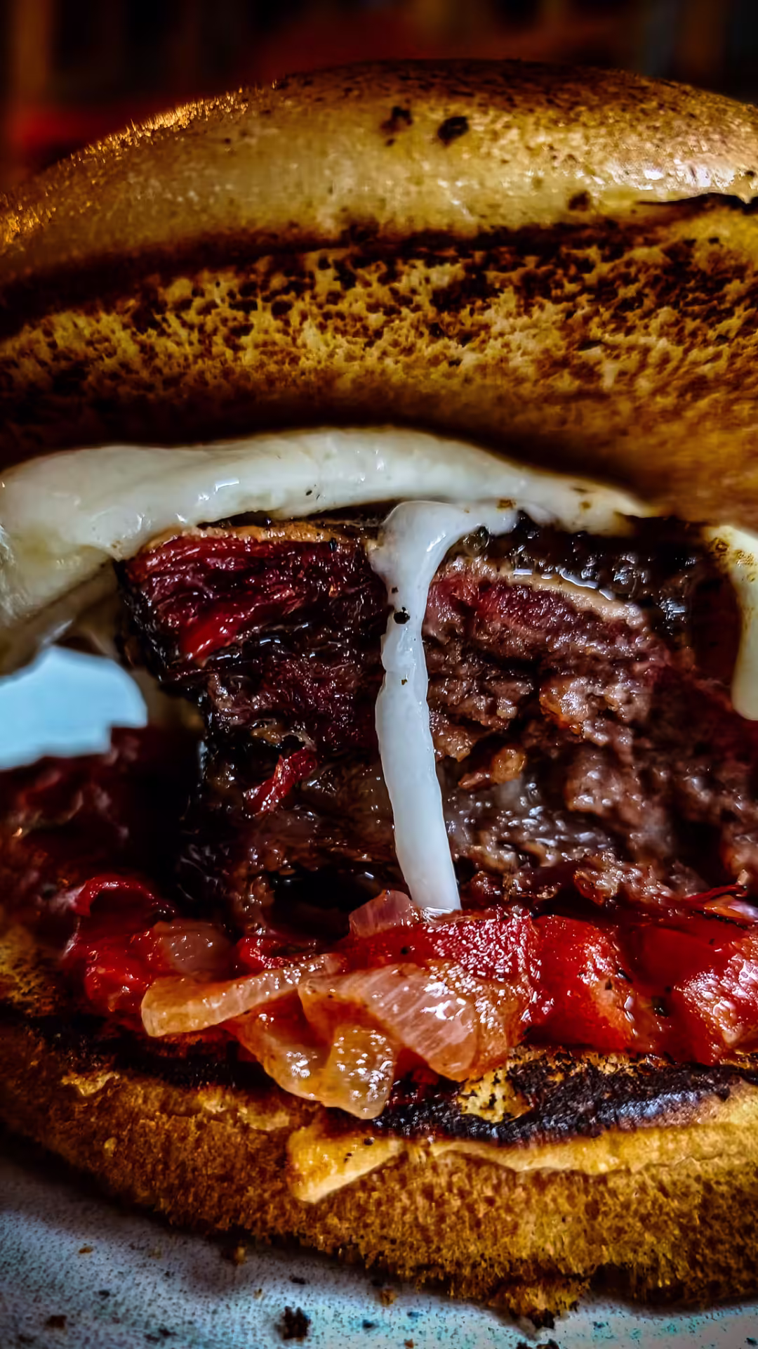 Close-up de hambúrguer artesanal com costela, queijo derretido, pimentões assados e pão tostado