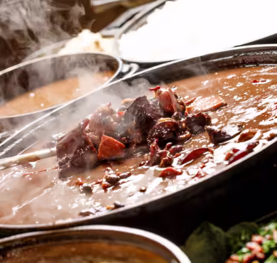feijoada Panela grande com carne cozida em molho escuro com pimentas e vapor subindo