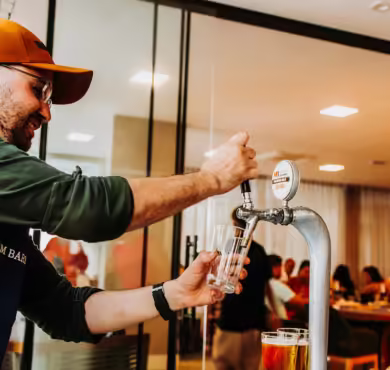 Garçom uniformizado servindo chope artesanal em torneira de chopp durante evento premium
