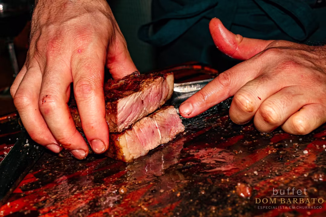 Mãos cortando picanha grelhada ao ponto sobre tábua de corte no buffet Dom Barbato
