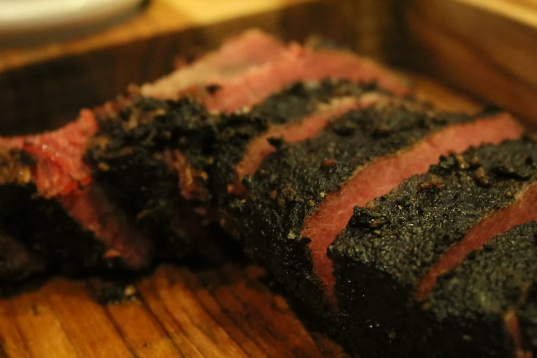 Fatias de brisket defumado com crosta negra escura sobre tábua de madeira
