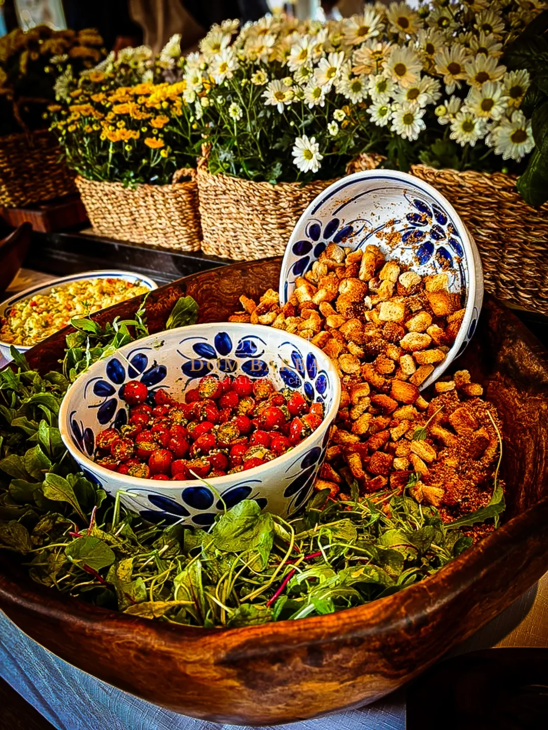 Tigela de madeira com folhas verdes, tomate cereja em pote azul e branco, torresmo e croutons