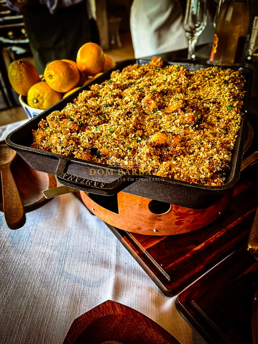 Bandeja de arroz com farofa dourada em churrasqueira, ao lado de tigela com limões sicilianos
