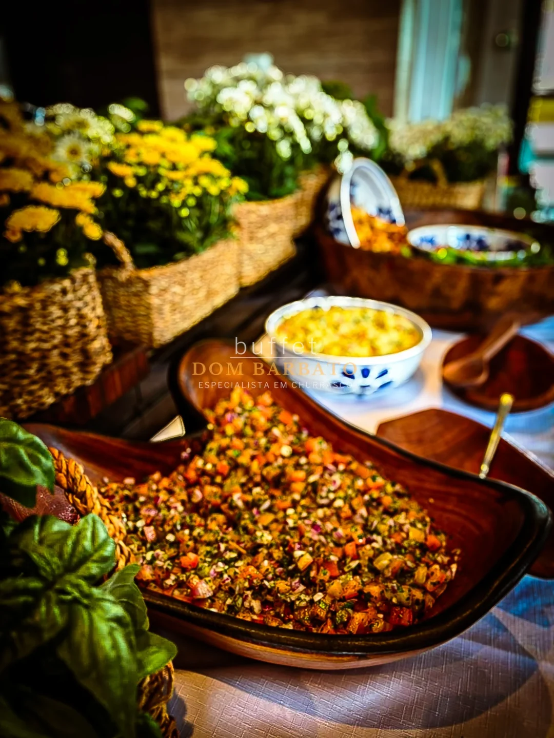 Bowl de madeira com vinagrete de tomate e cebola picados, ao fundo flores brancas e amarelas em cestos