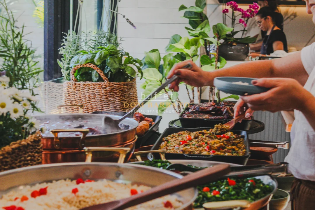 Buffet com panelas de cobre, arroz, farofa com pimentão, folhas verdes e carnes; pessoa servindo prato azul
