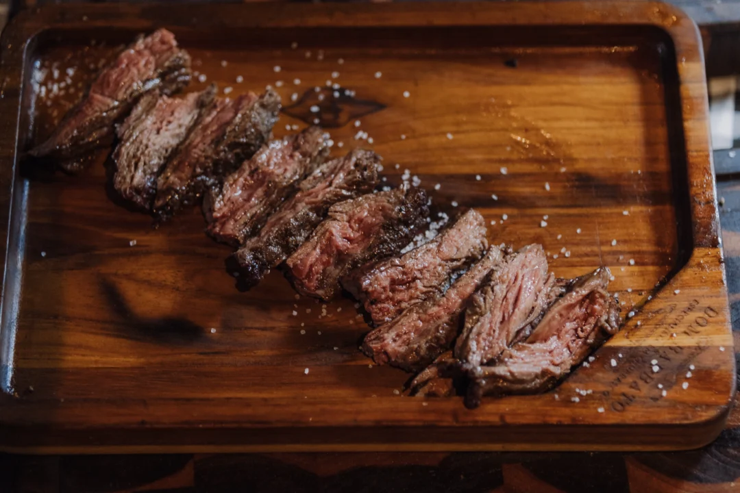 Fatias de carne grelhada fatiada sobre tábua de madeira, temperada com sal grosso