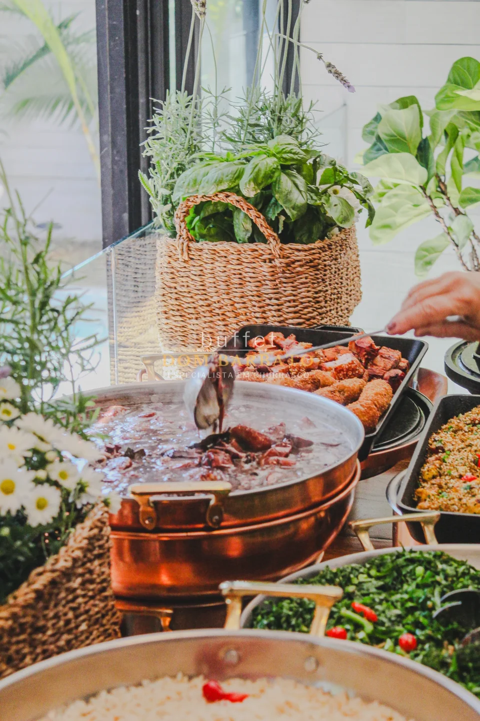 Panela de cobre com carnes cozidas, bandejas de carnes grelhadas e couve, cesta com ervas frescas