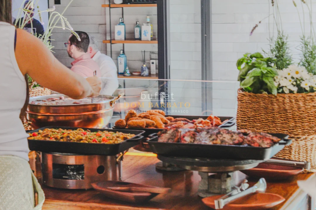 Bandejas de churrasco com carnes grelhadas, arroz, farofa e panela de cobre em buffet ao ar livre