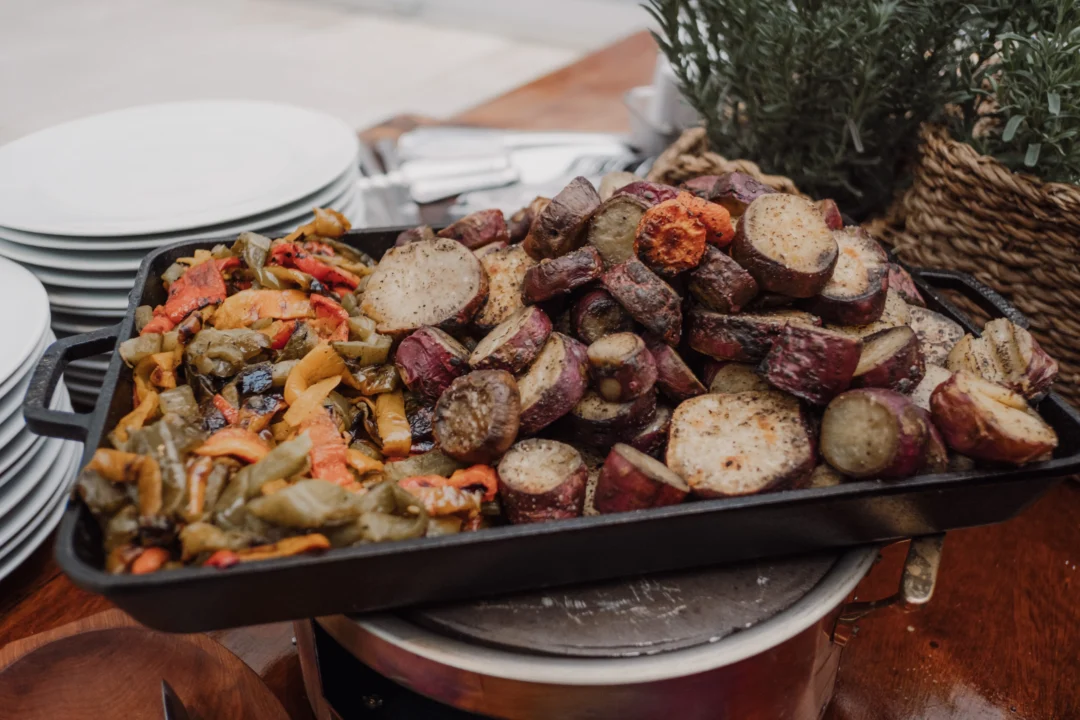 Bandeja de ferro com legumes assados e batata-doce grelhada, ao lado de pratos brancos empilhados