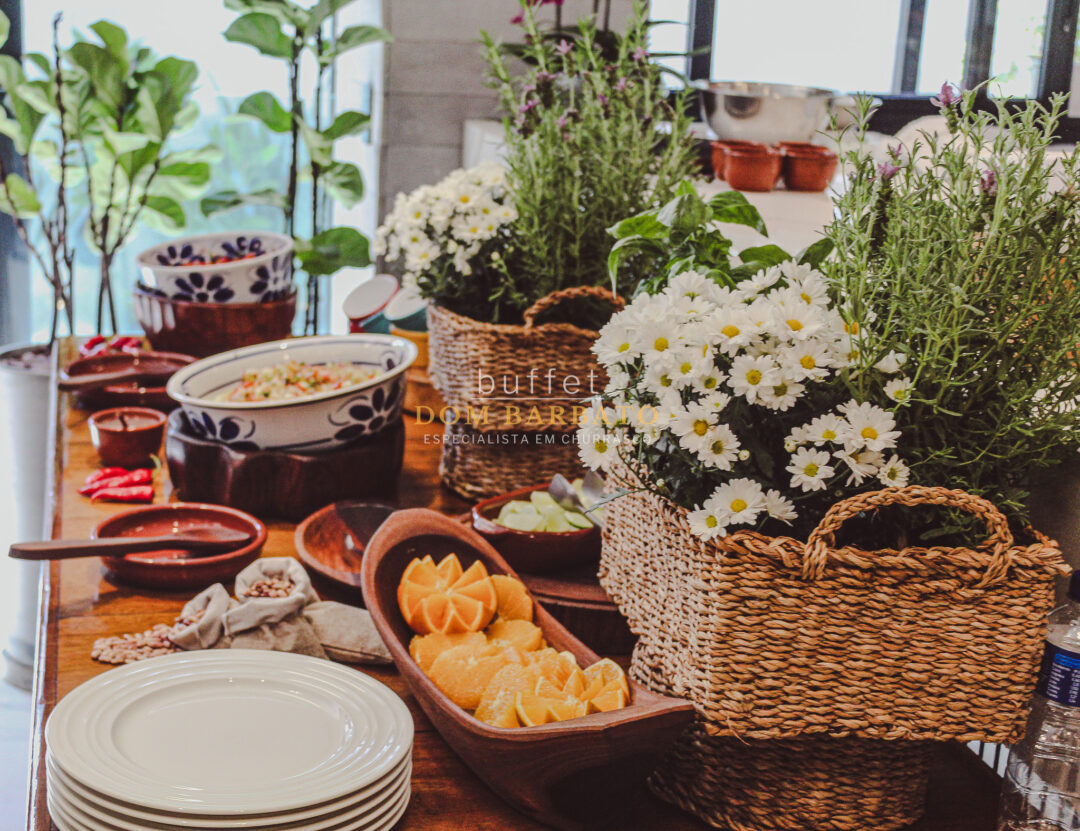 Mesa de madeira com laranjas fatiadas, pratos brancos, tigelas e cestas com flores margaridas brancas