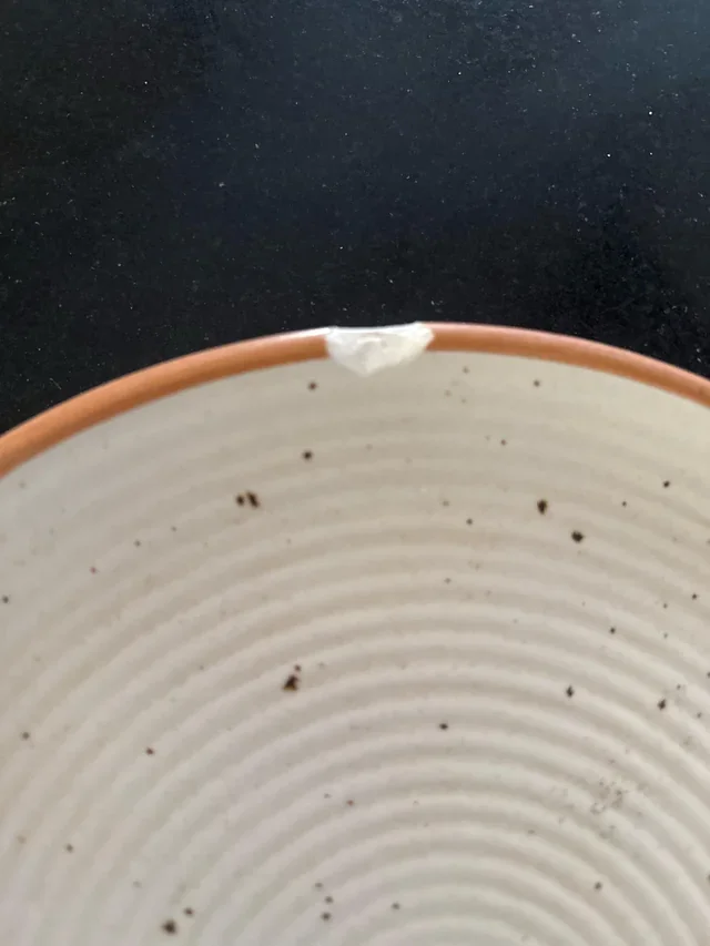 Borda de prato de cerâmica bege com textura estriada, detalhe de esmalte lascado revelando o barro terracota