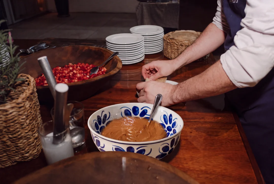 Mãos preparando doce de leite em tigela de cerâmica azul e branca, com tábua de morangos picados ao lado, mesa de madeira