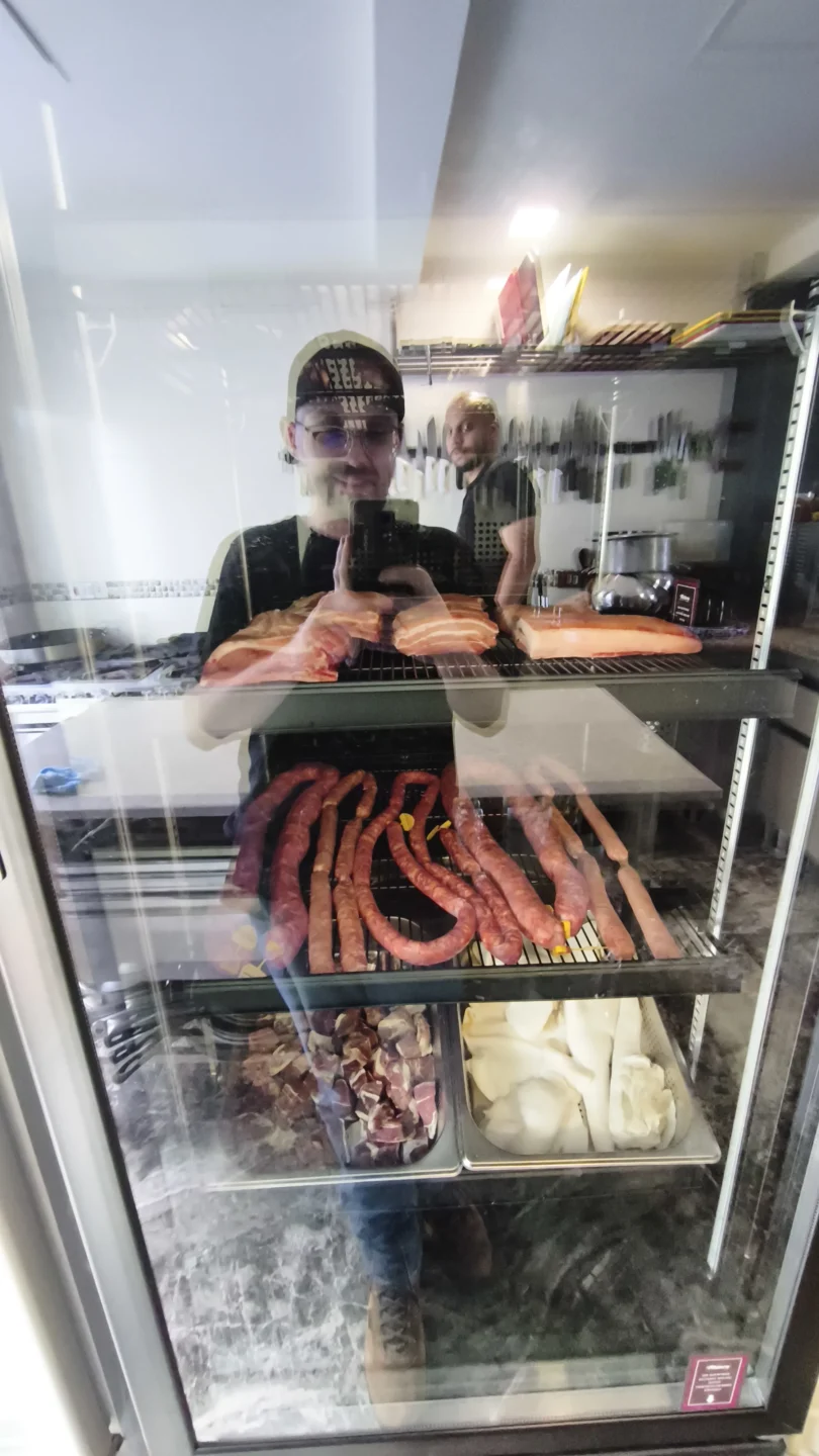 Homem fotografando expositor refrigerado com bacon, linguiças artesanais, carnes maturadas e coalhada em bandejas