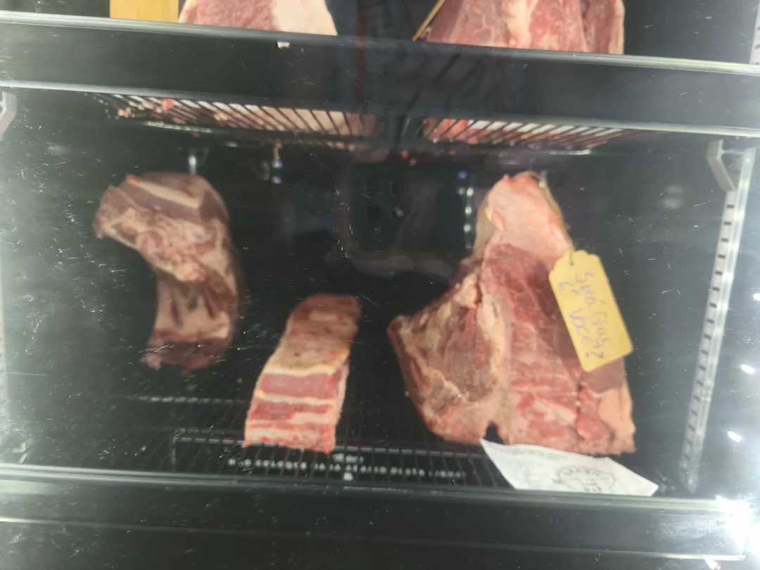 Peças de carne bovina em câmara de maturação com grades, etiqueta amarela manuscrita pendurada