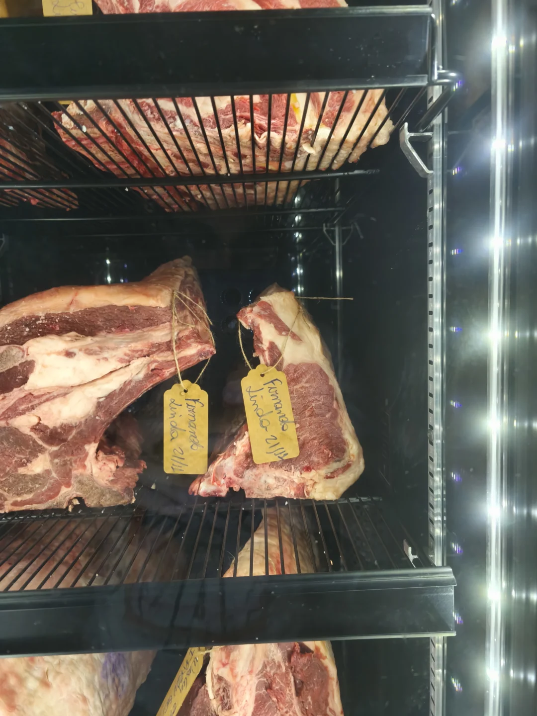 Peças de carne bovina com osso em grades de câmara refrigerada, com etiquetas amarelas penduradas