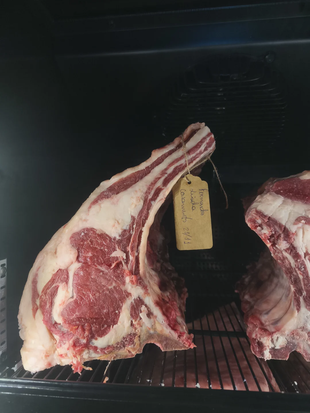Peça de costela bovina com capa de gordura em câmara escura, etiqueta de papel pendurada